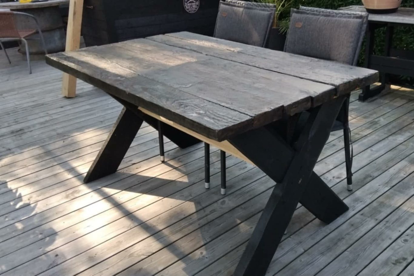 Bord Svart träbord med såriga ytor, placerat på en träbelagd uteplats.
